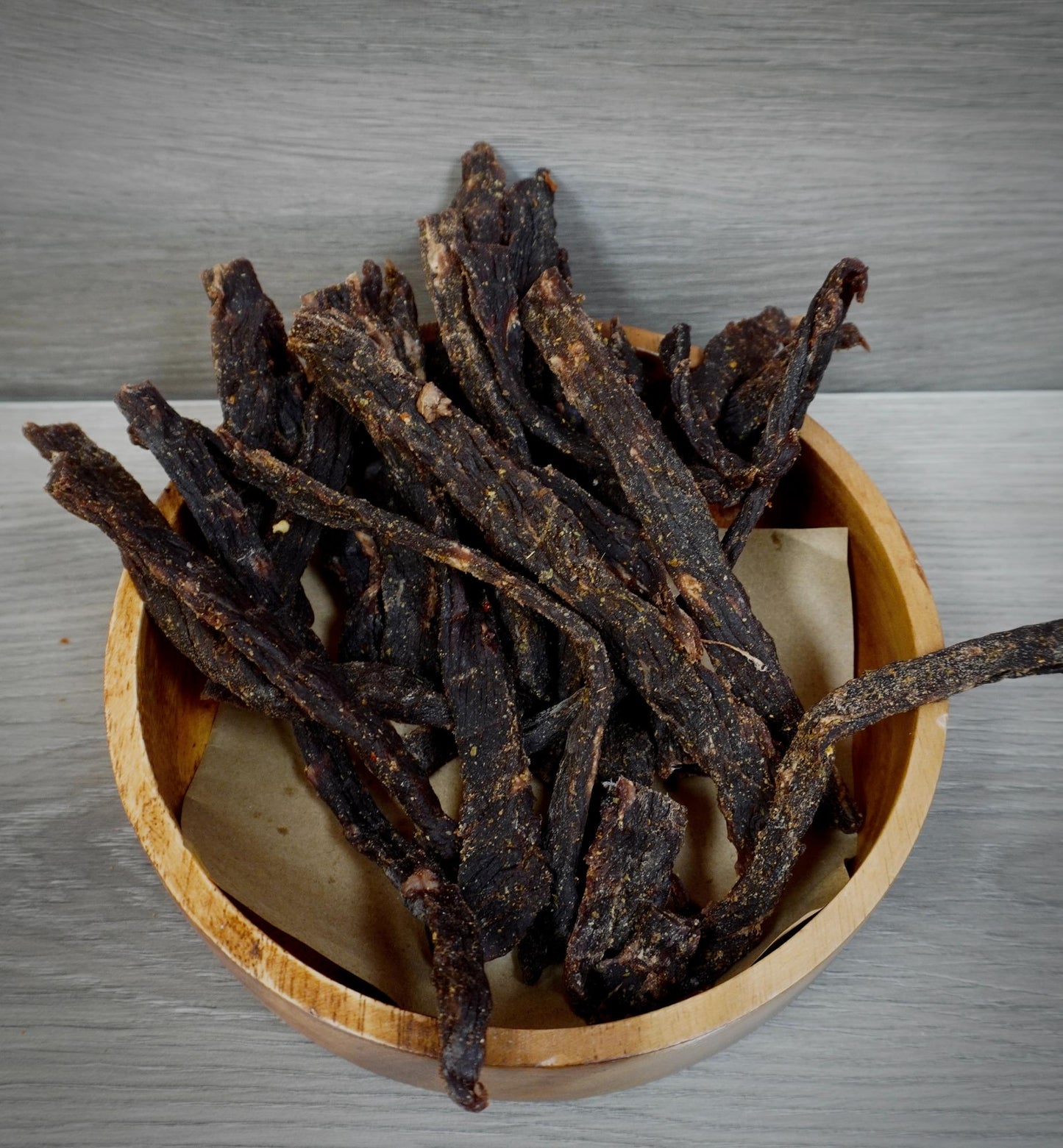 Dried beef jerky in a wooden bowl on a metallic surface