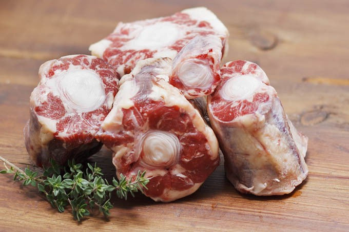 Raw beef bones with a sprig of thyme on a wooden surface